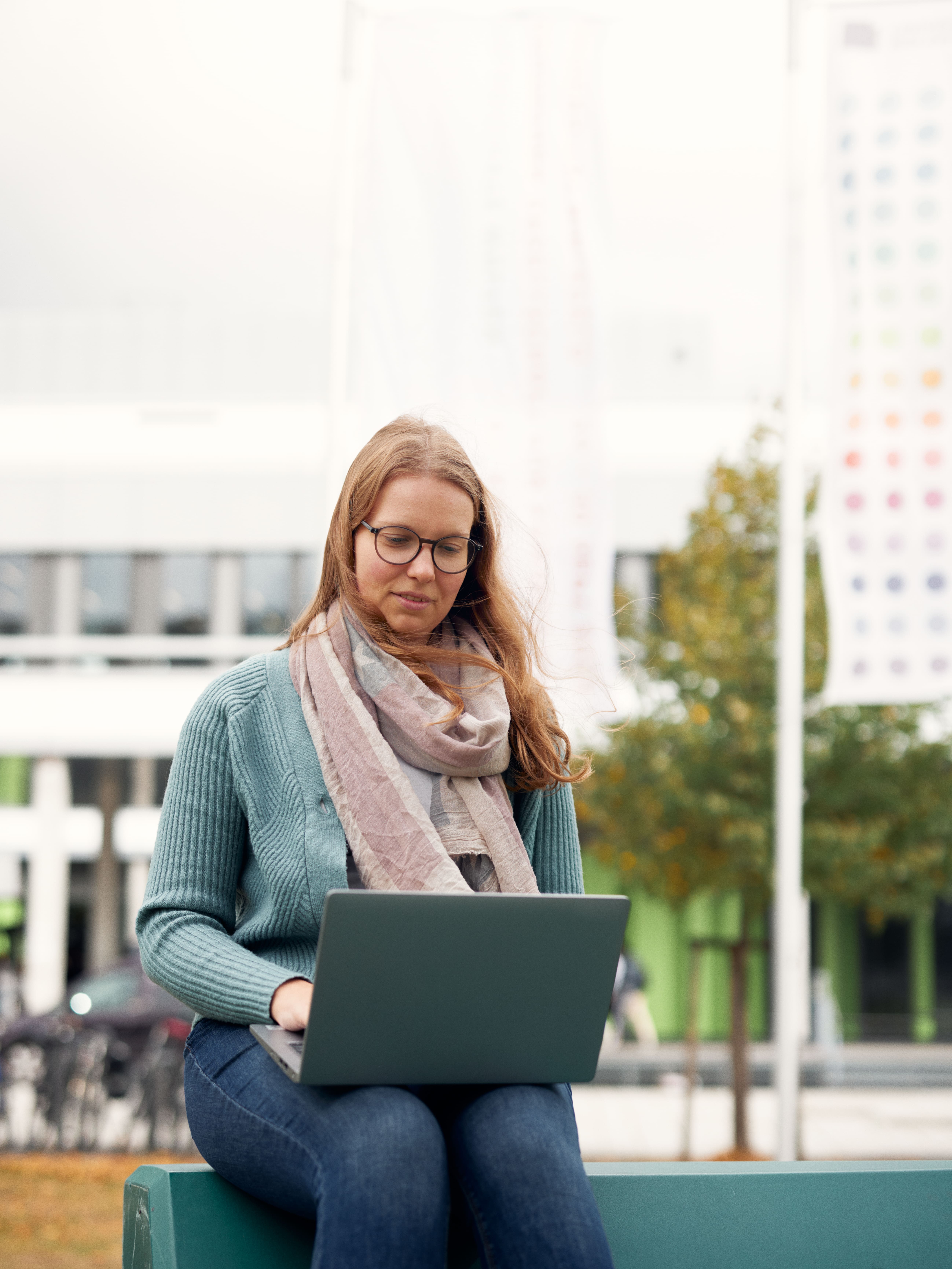 Eine Frau sitzt auf der Uni-Wiese und blick auf einen Laptop.