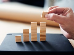 Symbolbild Evaluation - eine Hand baut kleine Türme aus Holzklötzen