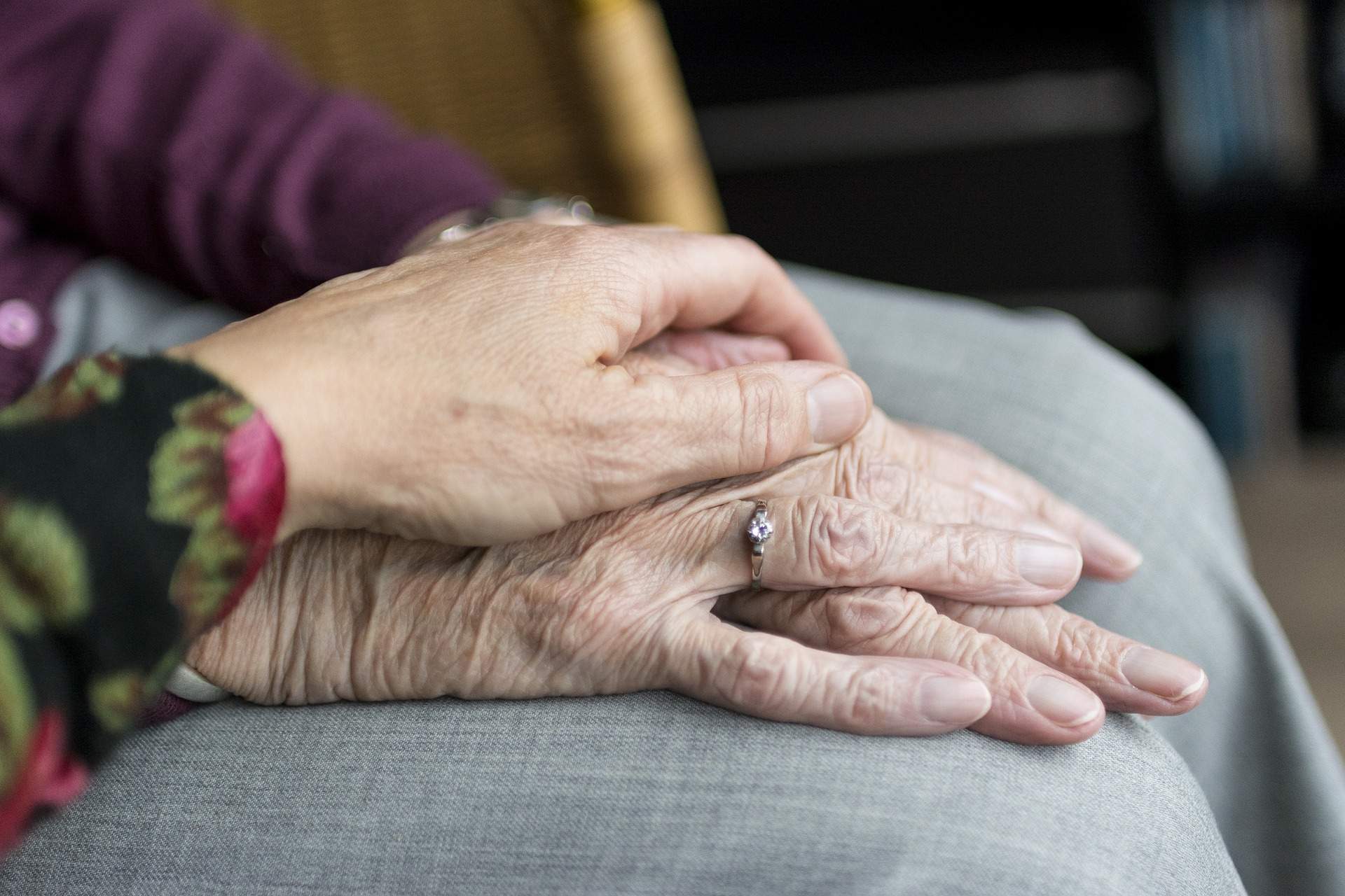 Eine Hand liegt fürsorglich auf den Händen einer älteren Person.