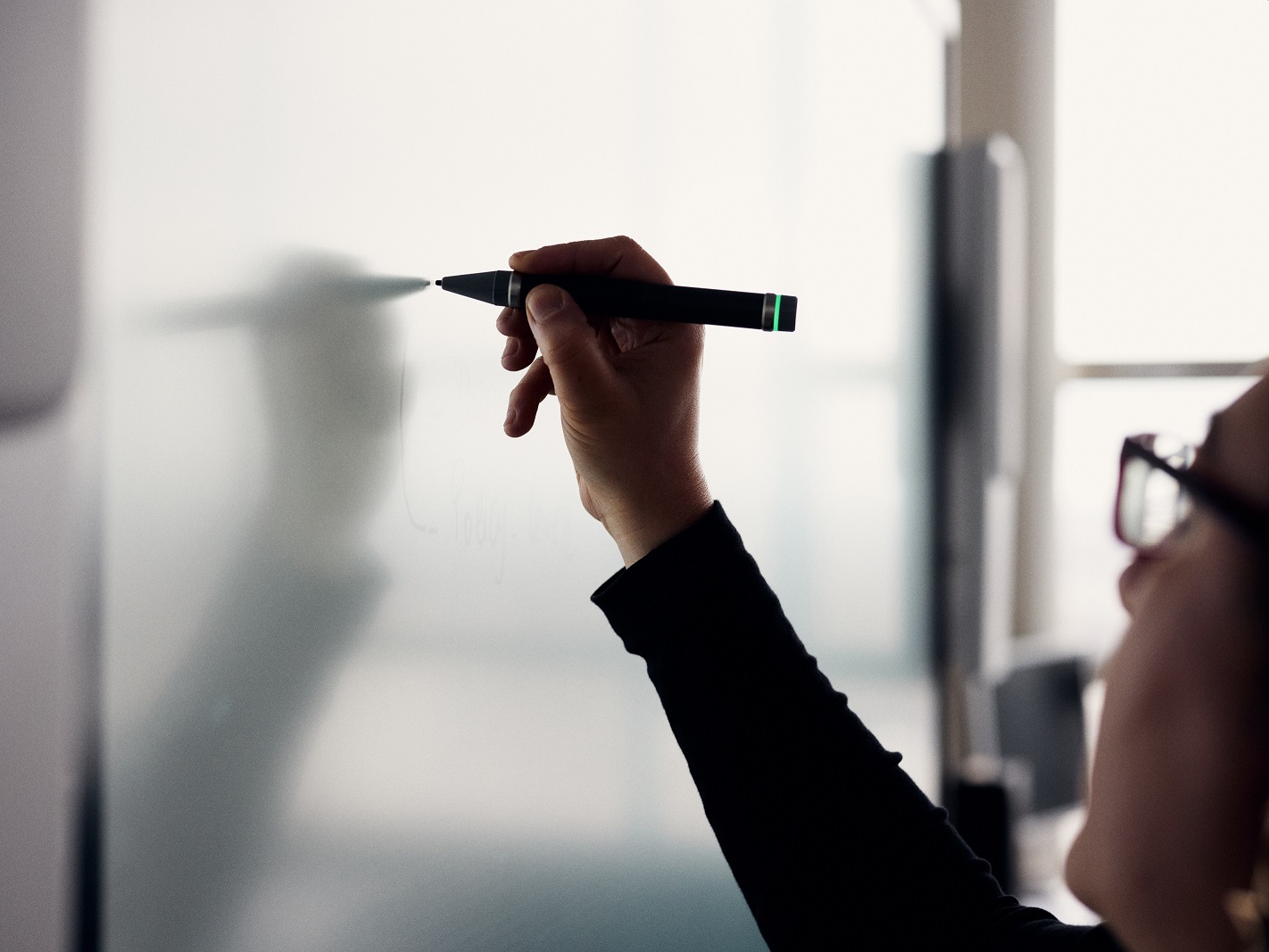 Hand einer Person, die mit einem Stift auf eine weiße Tafel schreibt