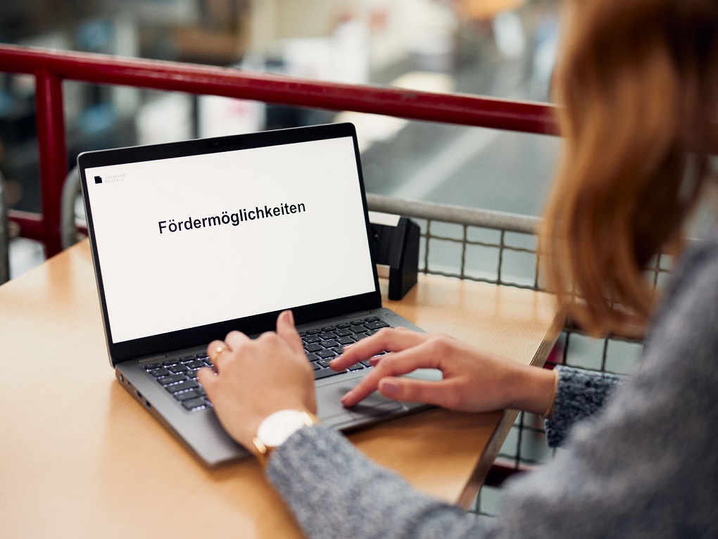 Eine Person sitzt am Laptop, auf dessen Bildschirm "Fördermöglichkeiten" zu lesen ist. 