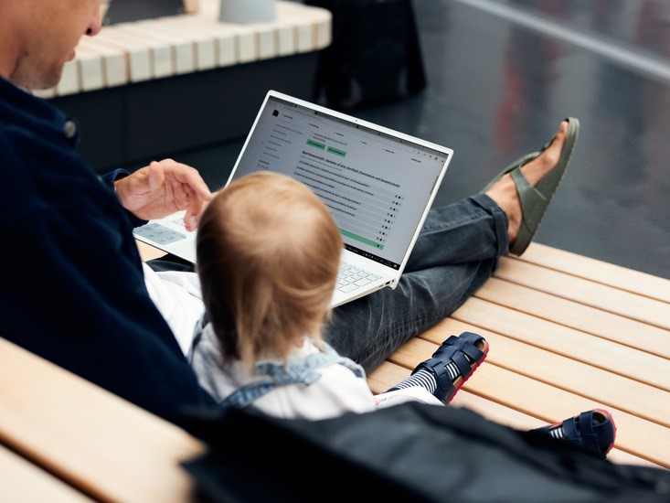 Vater sitzt mit Kind und Laptop in der Unihalle