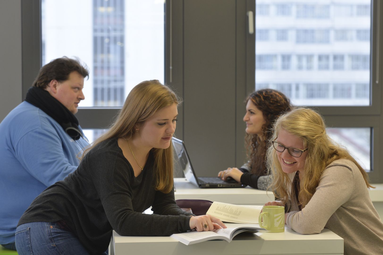 Zwei Studentinnen sitzen gemeinsam ber ein Buch gebeugt an einem Tisch