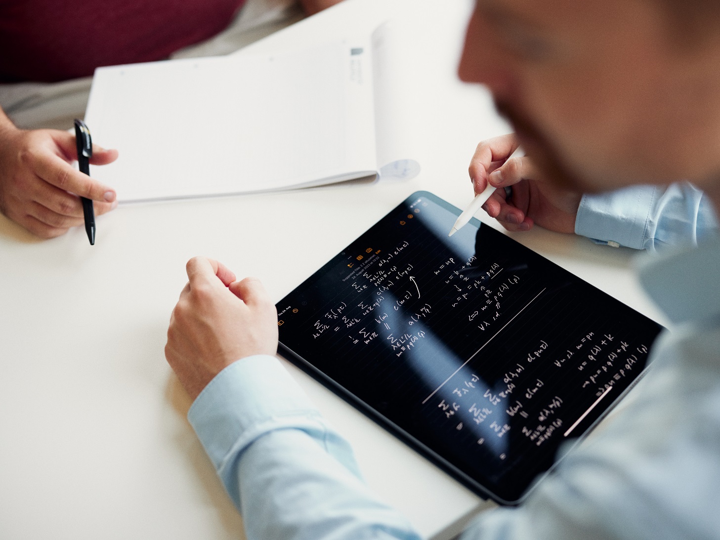 Mann in blauem Hemd schreibt mathematische Formeln auf ein Tablet