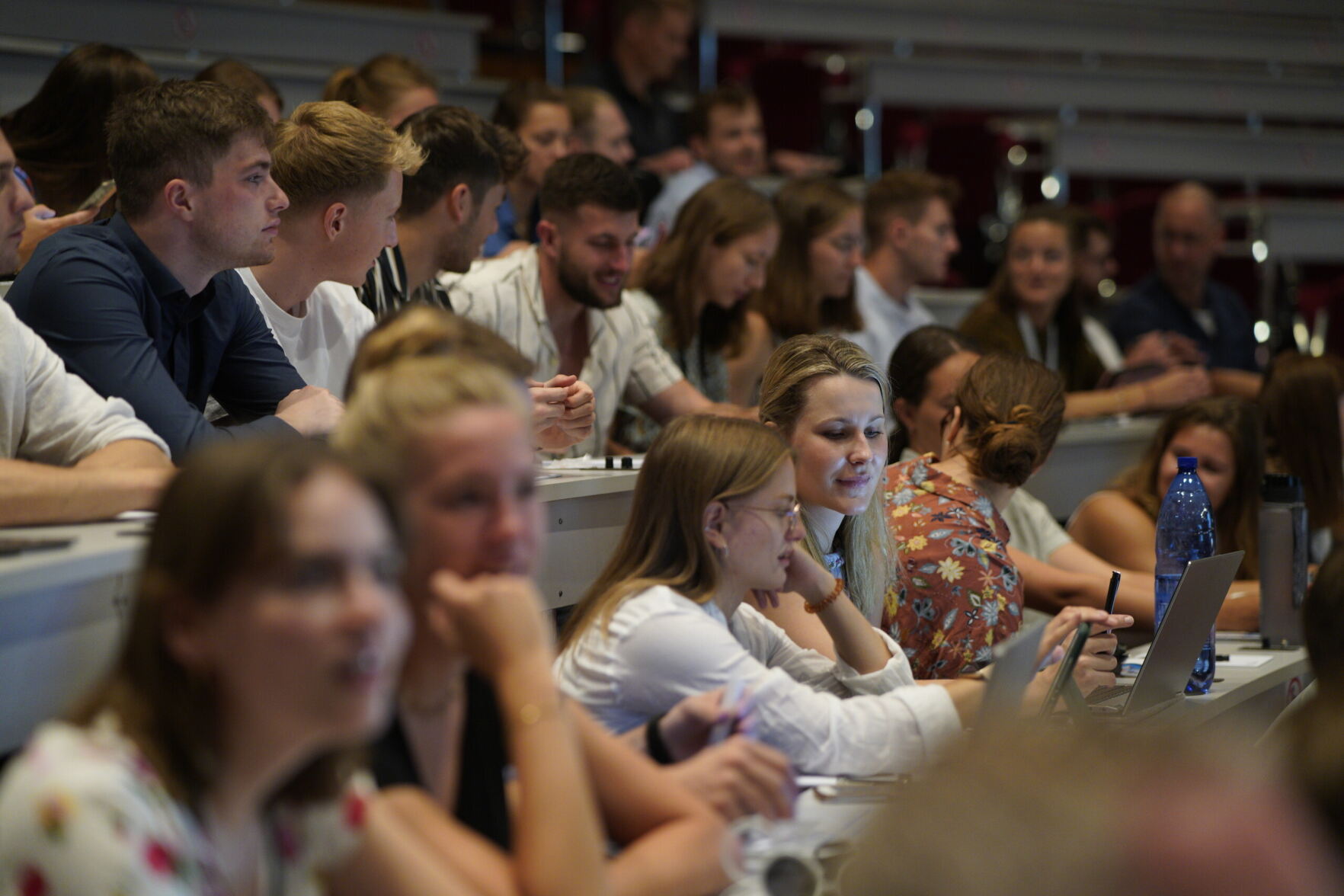 Viele Personen sitzen in einem Plenarsaal und unterhalten sich