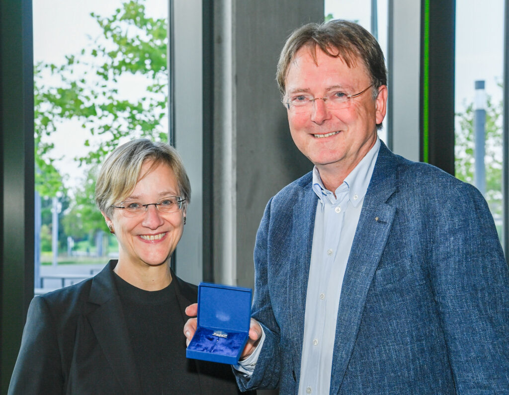 Prof. Dr. Angelika Epple und Prof. Dr. Fred Becker, der die verliehene Ehrennadel in die Kamera hält