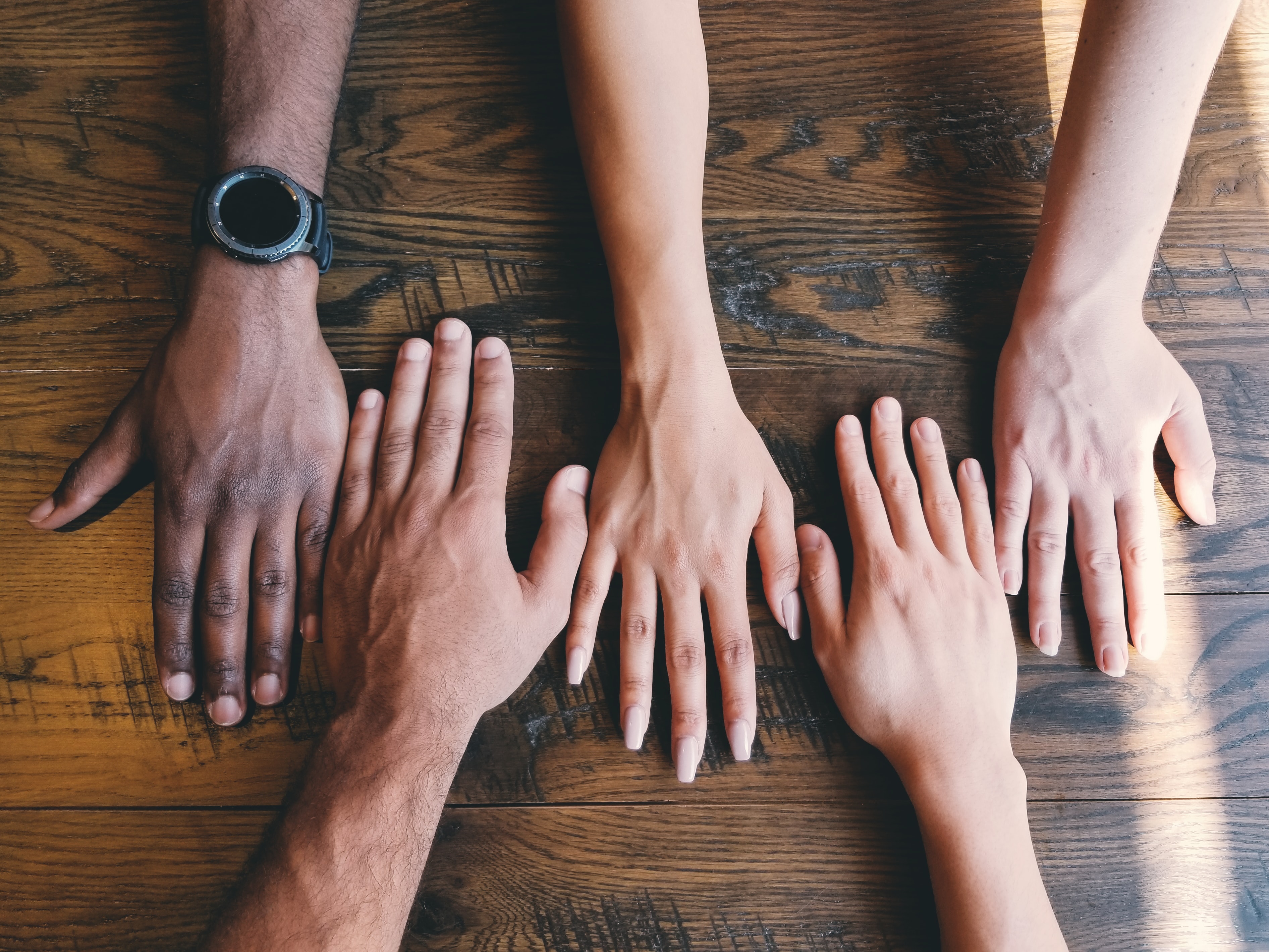 four hands of different colour and size laying on a wooden table